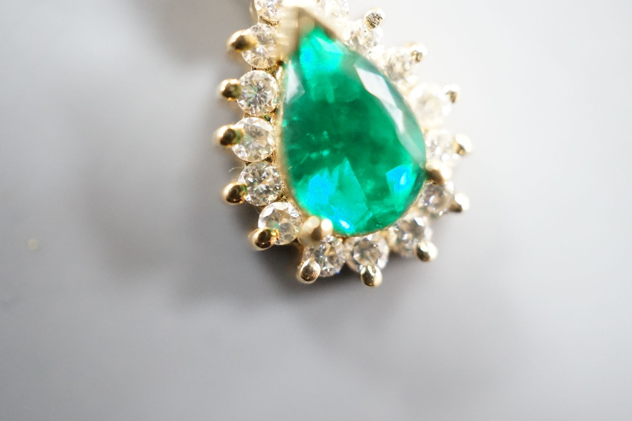 A modern 18k, emerald and diamond cluster set pear shaped pendant, overall 21mm, on an 18k chain, 43cm
